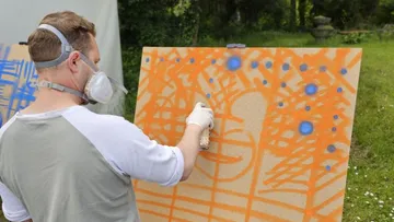 Man sprays orange and blue paint onto a board.