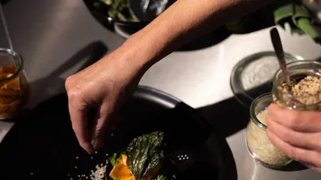 Hand sprinkle spice over a dish on a plate.