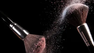 Two brushes spread colored powder against a black background.