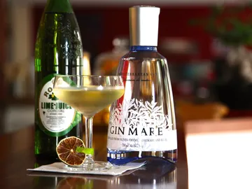 Cocktail glass with green drink surrounded by bottles