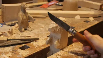 Wooden figure is worked with a knife in a workshop.