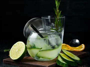 Drink in a glass with cucumber and lime on wooden board.