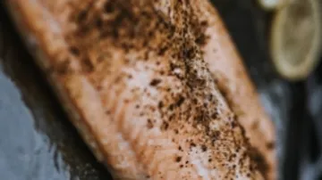 Lachsfilet mit Gewürzen auf einem dunklen Teller.