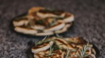 Grilled flatbreads are on a table with rosemary.