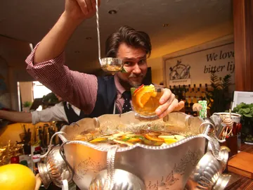 Bartender holds a drink and scoops from a bowl.