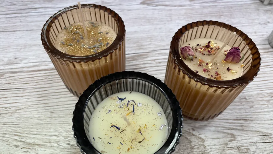 Drei Kerzen, dekoriert mit Glitzer und Blüten, stehen zusammen.