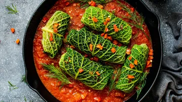 Cabbage rolls lie in tomato sauce in a pan.