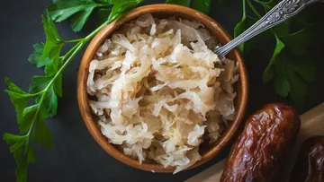 Bowl of sauerkraut and sausages on a dark background.
