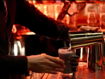 A bartender pours a drink into a glass.