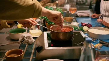 Pots on the stove, hands stir in the sauce.