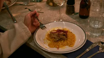 A hand holds a fork while eating risotto.