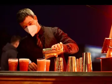 Bartender pours out drinks at an illuminated bar.