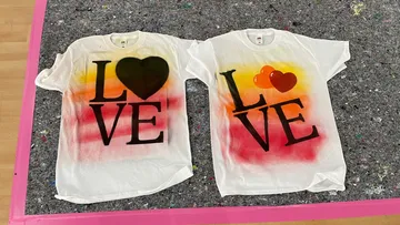 Zwei T-Shirts liegen auf einem grauen Untergrund, bedruckt mit `LOVE`.