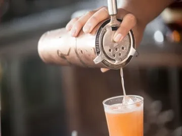 A bartender pours a drink into a glass.