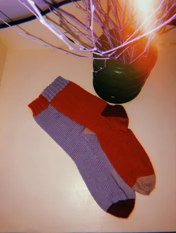 Bunte Socken liegen auf einem Tisch neben einer Vase.