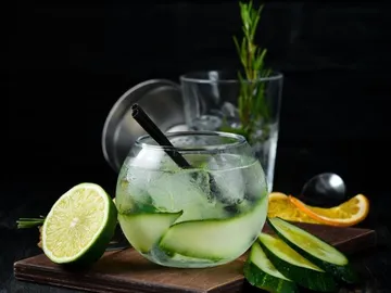 Glass with drink, ice cream and cucumber slices on wooden plate.