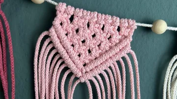 Pink macrame decoration hangs on a wall, artfully woven.