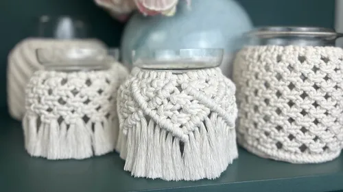 Makramee-Überzüge umgeben Glasbehälter auf einem Regal.