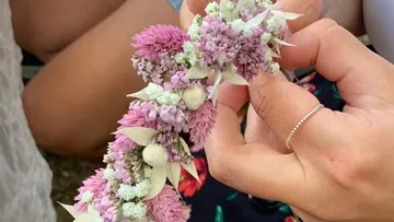 Blumenkranz wird von einer Hand gehalten, umgeben von Personen.