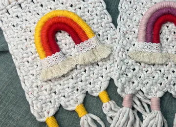 Farbenfrohe Regenbogen aus Garn auf grauem, gehäkeltem Material.