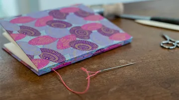 The manual is open, needle and thread next to it on the table.