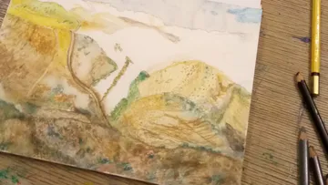 Painting of hills, with watercolors, on a table.