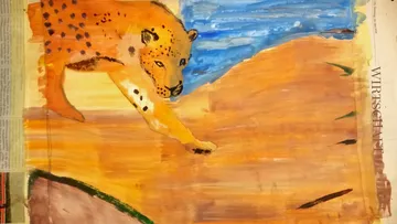 Ein Gepard läuft über eine sandige Fläche mit Wasser.