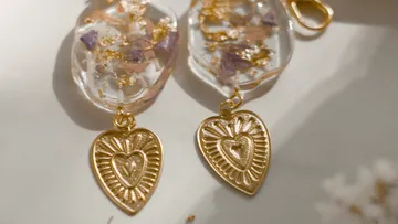 Goldene Ohrringe hängen an einer Oberfläche mit Blumen.