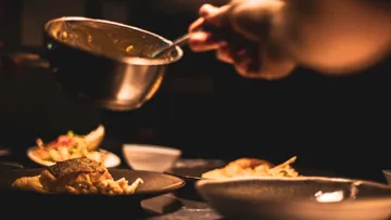 A hand pours sauce onto a plate in a restaurant.