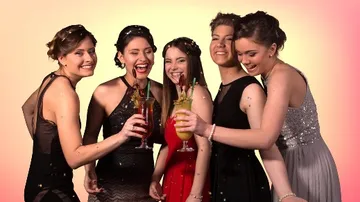 Five women toast with drinks in elegant clothing.