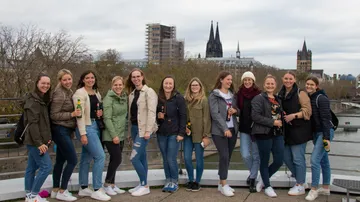 Group of women holding drinks at the riverbank, city view.