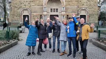 Gruppe von Menschen feiert vor historischem Gebäude im Freien.