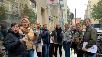 Gruppe von Menschen hält Flaschen vor Biermuseum in Stadt.