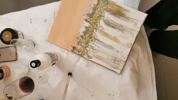 Canvas with paints, glasses and brushes on surface.