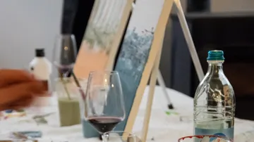 Painting is on easel, alcohol drinks on table.