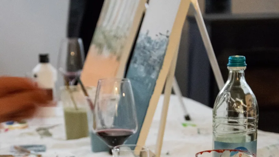 Gemälde steht auf Staffelei, Alkoholgetränke auf Tisch.