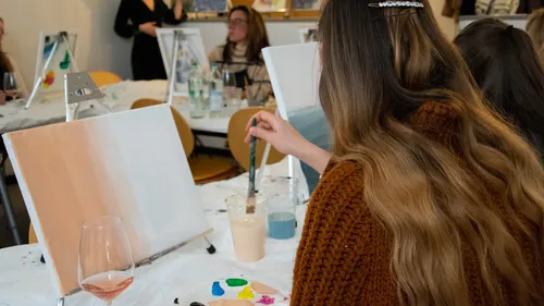 Frau malt mit Pinsel auf Leinwand in kreativer Umgebung.