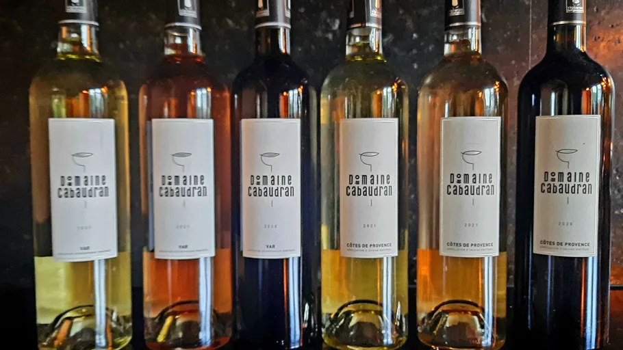 Six wine bottles are placed side by side on a shelf.