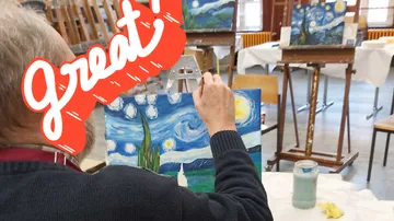 A man enthusiastically paints a picture in a studio.
