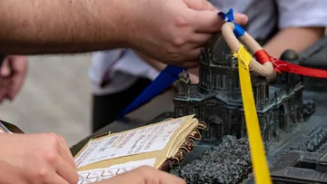 Hände halten Ringe über ein Miniaturgebäude auf Tisch.
