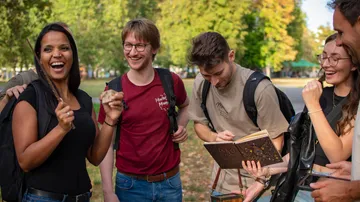 Gruppe von Freunden lacht und zeigt ein Buch im Park.