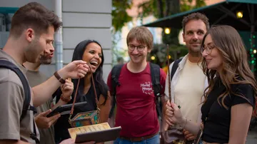 Six people smile while looking at a book.