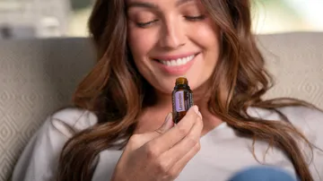 Woman smiles and holds a bottle of lavender oil.
