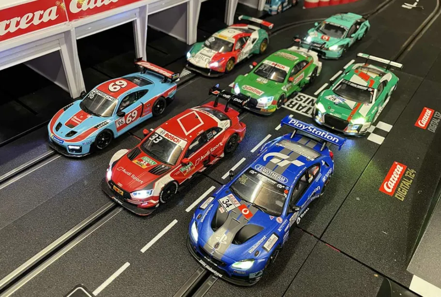 Slot cars drive on a racetrack in a pit stop area.