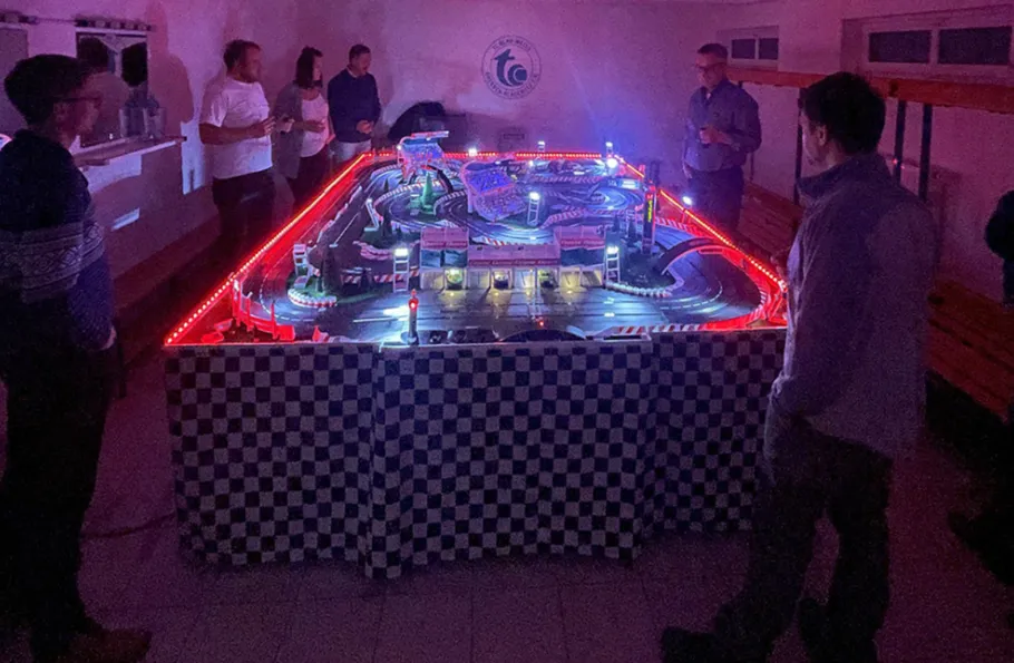 Electric racetrack lights up while spectators stand around them.