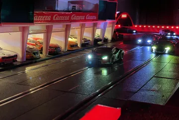 Model cars drive on an illuminated racetrack surrounded by boxes.
