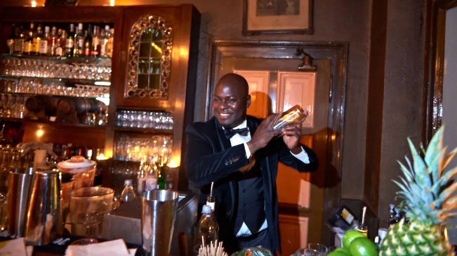Bartender shakes a cocktail behind the bar at a drink service.