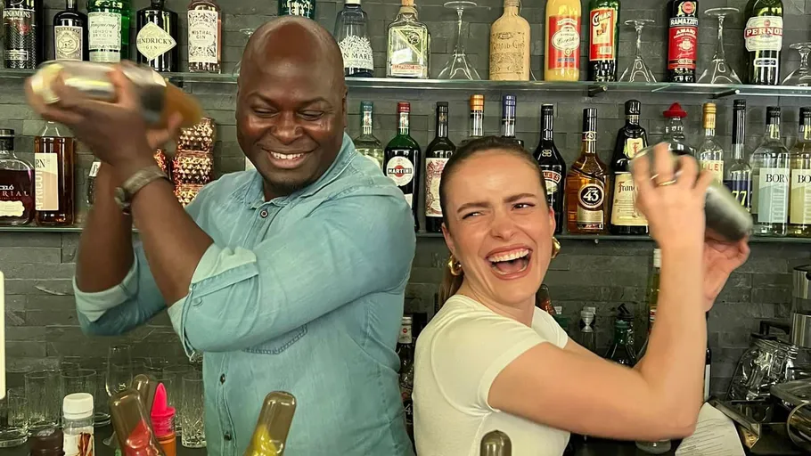 Two bartenders shake cocktails behind a bar full of spirits.