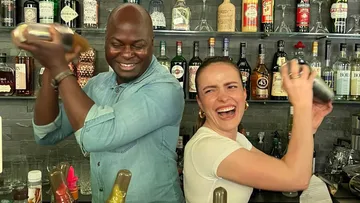 Zwei Barkeeper schütteln Cocktails und lachen hinter der Bar.