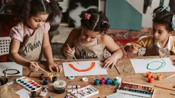 Three children draw creatively with colors at a table.